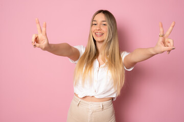 Wall Mural - Smiling pretty young woman showing thumbs up isolated over pink background