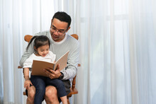 Asian Father Reading Storybook To Daughter In Living Room, Family Concept And Early Childhood Development