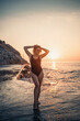 © Дмитрий Ткачук - Beautiful young woman in a black swimsuit alone on the beach by the sea at sunset. An adult slender girl resting on the ocean shore at sunset. Summer vacation concept. Selective focus