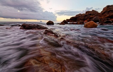 Wall Mural - Beautiful sunrise scenery of a rocky beach on northern coast of Taiwan, with golden sun rising on distant horizon & turbulent waves beating on rugged rocks under dramatic dawning sky (Long Exposure)