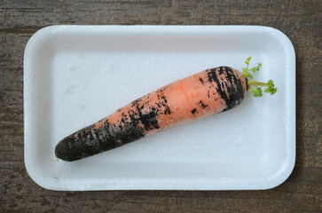 Top view of a carrot with black root rot on a single-use plate on a wooden table