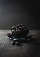 Black Bowl Of Blackberries On Wooden Table With Black Background.