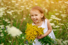 Sweet Naughty Red-haired Girl Laughs Merrily With Mouth Open. Baby Holds In Hands A Bouquet Of Their Yellow Wildflowers, Collected As A Gift To His Mother. World Happiness Day. Child's Day