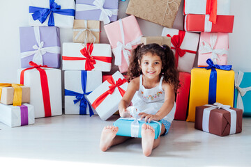 beautiful curly little girl opens gifts for the holiday