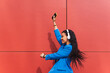 © Dani D.G - Girl dancing nonchalantly in the air in an urban scene. Woman on a red background, happy and crazy, dressed in retro 90s style blue clothes.