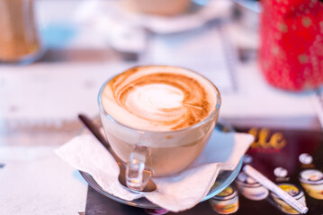 Wall Mural - Closeup of a cup of hot aromatic cappuccino coffee with a spoon next to it at a cafe