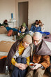 Vertical portrait of Caucasian senior couple hiding in refugee shelter covered with blanket on floor