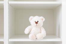 Smiling White Teddy Bear Sitting On Shelf In Wardrobe. Closeup. Front View.