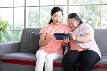 Wall Mural - mother using tablet computer with a girl down syndrome or her daughter, smiling and enjoying on sofa