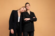 © Andrii - Two young business woman dressed black suit standing studio orange color background