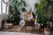 Freelancer woman enjoy remote work in cozy home office in indoor garden. Happy florist businesswoman outstretch arms after buying house plants online on laptop. Entrepreneur designer complete project