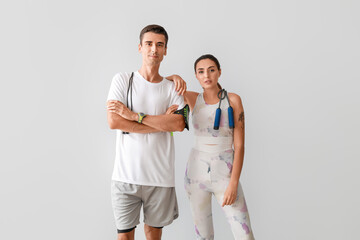 Poster - Sporty young couple with skipping ropes on grey background