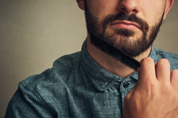 Poster - They cant resist the beard. Cropped shot of a handsome young man combing his beard against a grey background.