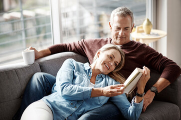 Poster - Weekends were made for winding down. Shot of a mature couple reading a book together while relaxing on the sofa at home.