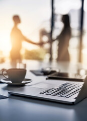 Aufkleber - Making smart business moves. Closeup shot of a laptop on a desk with businesspeople shaking hands in the background.