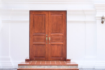 Closed brown wood door on white concrete wall background with lantern hanging