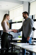 © JustLife - Colleagues handshake in office. Businesswoman and businessman discussing work in office.