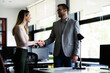© JustLife - Colleagues handshake in office. Businesswoman and businessman discussing work in office.