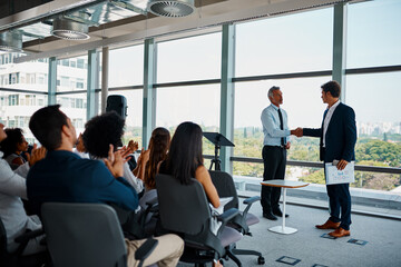 Poster - Congratulations on a job well done. Full length shot of two businessmen shaking hands in front of an audience during a seminar.