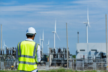 engineer at work. Young  engineer working in wind turbine farm on blue sky background. Young  engineer working on substation and  wind turbine farm on blue sky background.