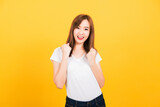 Fototapeta Do pokoju - Asian happy portrait beautiful cute young woman teen standing wear t-shirt makes raised fists up celebrating her success looking to camera isolated, studio shot on yellow background with copy space
