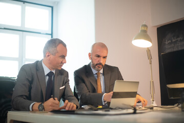 Portrait of successful businessmen in office. Two serious man in suits working with computer at table, making decisions and developing strategy for business growth. Business growth and finance concept