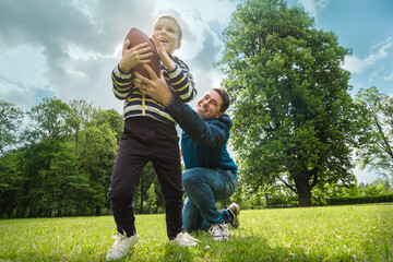 Father and son playing football, Father's day, Playful Man teaching Boy rugby outdoors in sunny day at public park. Family sports weekend.