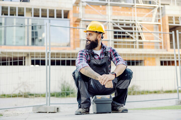 Wall Mural - A worker sitting on a toolbox and waiting for a ride at construction site.