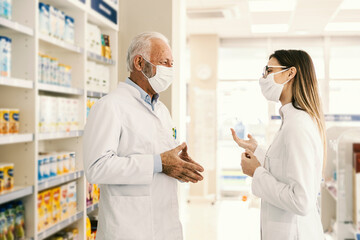 Wall Mural - An old and young colleagues standing at pharmacy during corona virus and discussing,