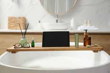 Wall Mural - Wooden bath tray with tablet, face roller and cosmetic products on tub indoors