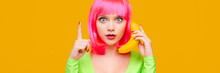 Surprised Young Sexy Woman On Pink Wig Call By Banana And Shows Up Finger On Yellow Background
