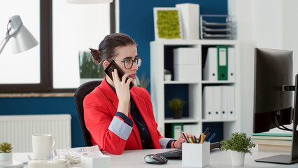 Wall Mural - Business woman using smartphone to talk on phone call about financial growth in startup office. Marketing analyst with e commerce expertise having remote conversation on mobile phone.