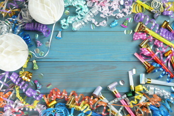 Frame of colorful serpentine streamers and other party accessories on light blue wooden background, flat lay. Space for text