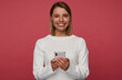 © timtimphoto - Studio portrait of young female student posing over red background, smiles broadly while typing message on her phone