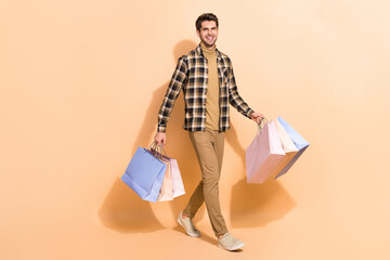 Poster - Full length body size view of attractive guy visiting store wearing checked shirt carrying bags isolated over beige pastel color background