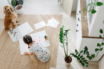 Wall Mural - A girl draws hearts for his mother sitting on carpet floor in living room, cocker spaniel dog sitting nearby