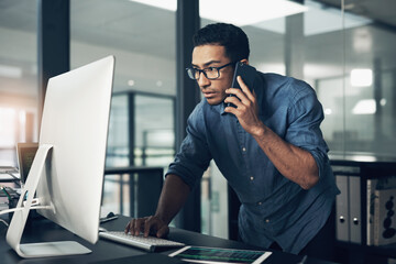 Canvas Print - One decision away from a better tomorrow. Shot of a young man using his cellphone while working on a computer in a modern office.