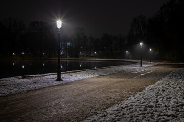 The Ducale park in the historic center of Parma during a winter night with snow along the promenade between the illuminated street lamps.