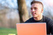 © Massimo Parisi - Portrait of attractive young office worker in casual wear, smiling in a break moment. He works remotely with the laptop from a table in the park, remote working concept