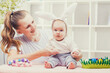 © Dmytro Titov - Happy Mother and baby with bunny ears playing Easter egg.