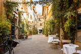 Fototapeta Uliczki - Beautifully landscaped narrow street with restaurant tables in the old town of Grosseto, in Maremma region of Italy. Cozy city view of the old Italian town