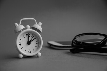 Alarm clock pointing at 2 o'clock with glasses, phone and black and white background. Copy space concept