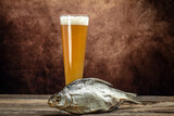 Fototapeta Boho - pour beer into a tall glass with a thick foam, dried fish on wooden background. Beer brewery concept. Snack for beer dried smelts. Beer background