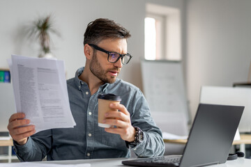 Poster - Mature man CEO of IT company sitting at workplace in front of laptop, reading report and looking at computer screen