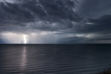 Lightning Bolts Reflection Over The Sea. Taken During A Thunderstorm Over The Ocean With Clouds In The Background