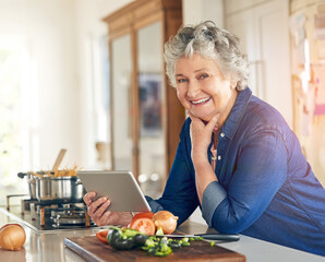 Wall Mural - This recipe even comes with a video tutorial. Portrait of a senior woman using a digital tablet while cooking in her kitchen.