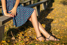 Cropped Image Of Slender Female Legs. Woman Sitting On A Wooden Bench In Autumn Park