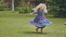 A Little Girl In A Dress Twirls In The Garden.