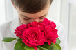 © Anna - Little boy's face hiding into big bouquet of red roses on white background, greetings and celebration concept, copyspace.