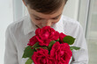 © Anna - Boy in white shirt hides his face in bouquet of red flowers on white background. Celebrations and greetings concept, holidays, romantic mood.